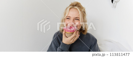 Close up portrait of happy, cute blond woman, holding doughnut, eating sweet, delicious comfort food, showing dessert at camera Close up portrait of happy, cute blond woman, holding doughnut, eating sweet, delicious comfort food, showing dessert at camera 113811477
