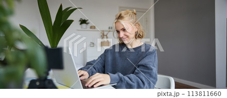 Portrait of young blond woman, female college student works from home on assignment, uses laptop, studies remotely, sits in room in front of computer Portrait of young blond woman, female college student works from home on assignment, uses laptop, studies remotely, sits in room in front of computer 113811660