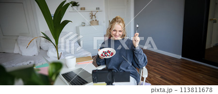 Portrait of cute young girl vlogger, showing her breakfast on camera, recording vlog in her bedroom, holding dessert, eating Portrait of cute young girl vlogger, showing her breakfast on camera, recording vlog in her bedroom, holding dessert, eating 113811678