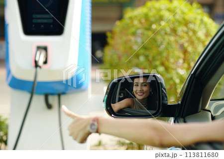 Happy ev driver showing thumbs up after charging electric car 113811680