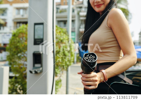Smiling woman holding electric car charging plug 113811709