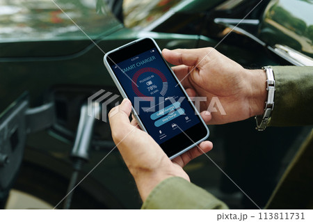 Electric car driver checking smart charger application on smartphone 113811731