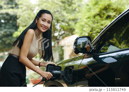 Portrait of smiling woman charging electric car after coming home 113811749
