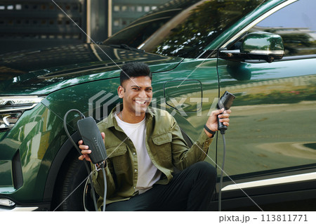 Happy man showing electric car charging cable with plug Happy man showing electric car charging cable with plug 113811771