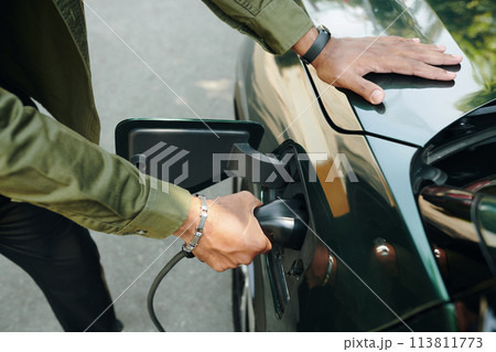 Closeup image of electric car owner putting plug in charge port 113811773
