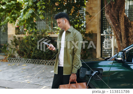 Serious man checking notifications on smartphone when walking from car to house entrance 113811786