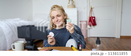 Portrait of young woman promoting beauty product, applies makeup in front of camera, recording video for her vlog, creating content for social media, sitting in a room on floor Portrait of young woman promoting beauty product, applies makeup in front of camera, recording video for her vlog, creating content for social media, sitting in a room on floor 113811855