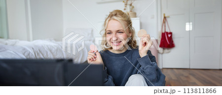 Portrait of young woman, beauty content creator, sitting in a room in front of digital camera, recording makeup tutorial vlog, showing cosmetic facial products Portrait of young woman, beauty content creator, sitting in a room in front of digital camera, recording makeup tutorial vlog, showing cosmetic facial products 113811866