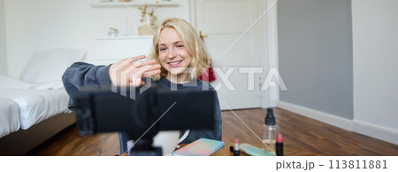 Close up portrait of happy young beauty blogger, records lifestyle vlog in her room, using camera with stabiliser, shows makeup brush and cosmetics 113811881