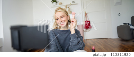 Portrait of content media creator, blogger sits in her room and records video of her favourite makeup brushes, talks on camera 113811920