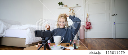 Portrait of stylish, smiling beautiful woman, recording lifestyle vlog, getting ready on camera, showing how to make her hairstyle for social media followers, vlogging from her room 113811979