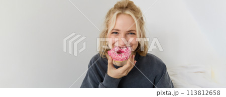 Portrait of cute blond girl holding pink doughnut with sprinkles on top, showing her favourite food Portrait of cute blond girl holding pink doughnut with sprinkles on top, showing her favourite food 113812658