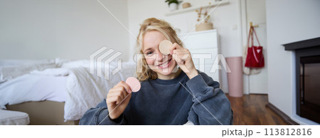 Portrait of young woman chatting on live stream about makeup, sits on floor in bedroom, showing beauty products to followers 113812816