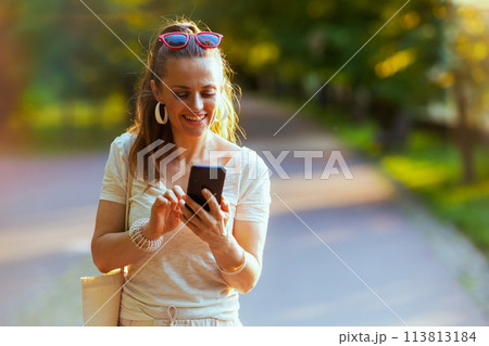 smiling trendy woman in shirt using smartphone and walking smiling trendy woman in shirt using smartphone and walking 113813184