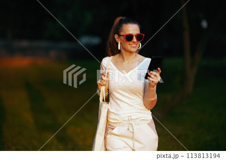 smiling elegant female in white shirt with smartphone walking 113813194