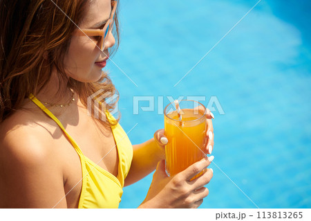 Young woman in yellow bikini drinking fresh juice by swimming pool Young woman in yellow bikini drinking fresh juice by swimming pool 113813265