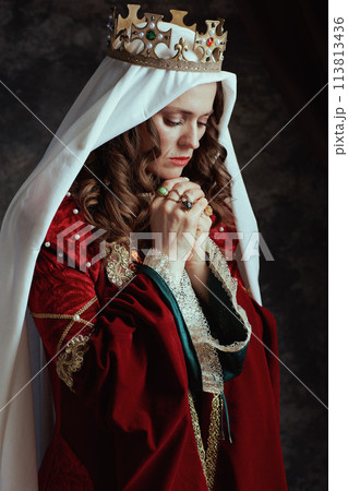 medieval queen in red dress with veil and crown praying 113813436