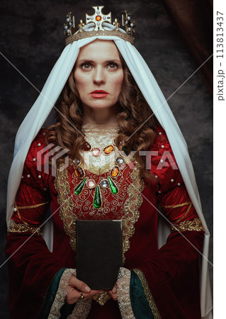 medieval queen in red dress with book, veil and crown 113813437