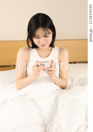 ベッドに座ってスマホを見る若い女性 ベッドに座ってスマホを見る若い女性 113814550