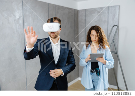 Man client wearing VR glasses imagining future interior standing with designer at the construction site. The concept of repair on a modern design. 113818882