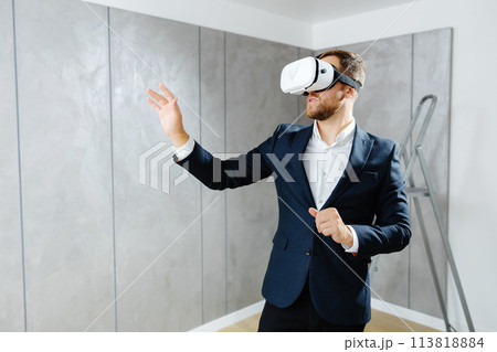 Young man wearing VR glasses, scrolling with hands in air using futuristic innovative technology choosing home design. Repair and renovation concept. Virtual reality Young man wearing VR glasses, scrolling with hands in air using futuristic innovative technology choosing home design. Repair and renovation concept. Virtual reality 113818884
