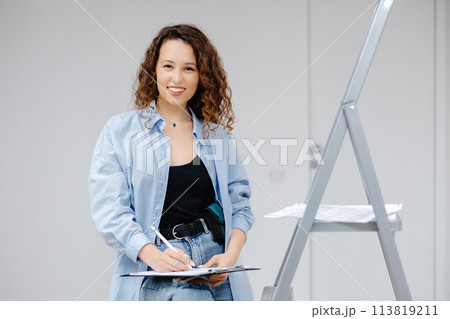 A young pretty girl designer keeps documents while standing at her workplace. Apartment renovation and design concept A young pretty girl designer keeps documents while standing at her workplace. Apartment renovation and design concept 113819211