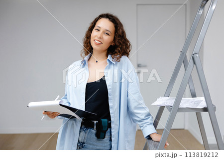 A young pretty girl designer keeps documents while standing at her workplace. Apartment renovation and design concept 113819212
