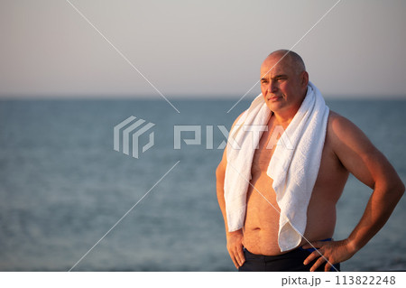 Elderly handsome man with a white towel on a background of the sea. Elderly handsome man with a white towel on a background of the sea. 113822248