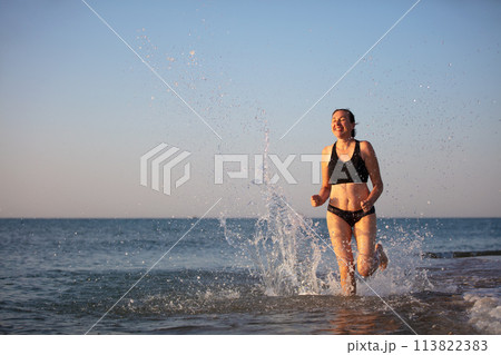 A middle-aged woman runs along the shore. Doing sports at sea. 113822383