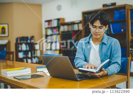 Male college students are working on laptops and searching for books to study, make reports, find useful information in college room. Concept of reading, learning and intelligence. 113822890