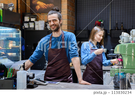 Colleagues partners young man and woman in aprons working together in coffee shop Colleagues partners young man and woman in aprons working together in coffee shop 113830234