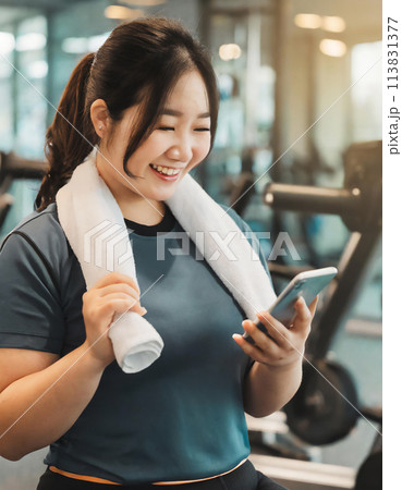 スマートフォンのアプリを確認しながらジムで運動する健康的な笑顔の女性 113831377