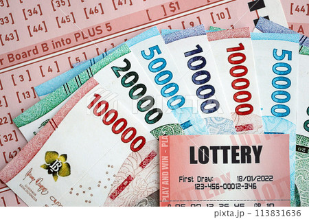 Red lottery ticket lies on pink gambling sheets with indonesian rupiah money bills. Lottery playing concept or gambling addiction in indonesia Red lottery ticket lies on pink gambling sheets with indonesian rupiah money bills. Lottery playing concept or gambling addiction in indonesia 113831636
