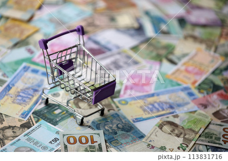 Supermarket trolley on many banknotes of different currency. Background of shopping worldwide close up Supermarket trolley on many banknotes of different currency. Background of shopping worldwide close up 113831716