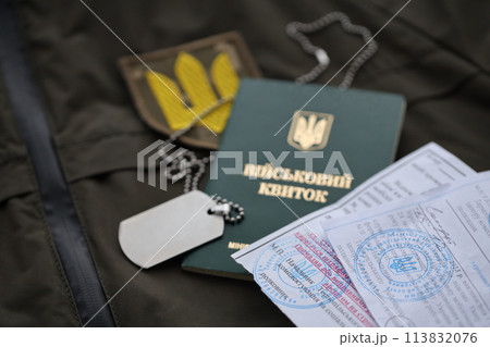 Military token or army ID ticket with mobilization notice lies on green ukrainian military uniform indoors close up 113832076