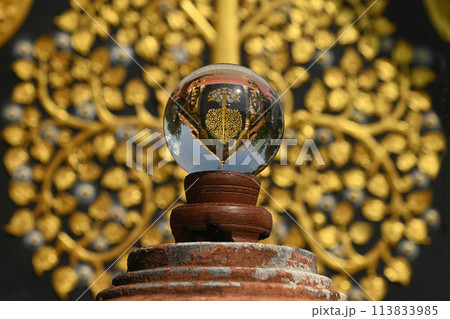 Glass ball placed on a decorative pole Reflecting Buddhist art on the Buddhist Church walls at Wat Phra That Doi Pra Chan temple. Located at Lampang Province in Thailand. 113833985