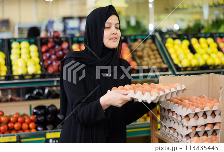 Asian girl in hijab buys chicken eggs in supermarket Asian girl in hijab buys chicken eggs in supermarket 113835445
