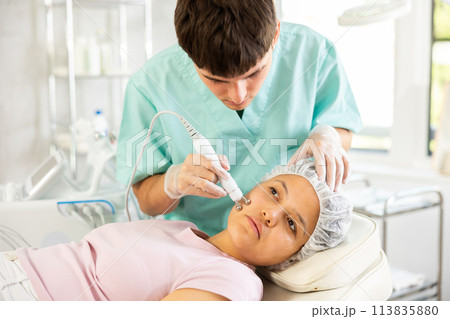 Young male cosmetologist doing microcurrent procedure to young woman Young male cosmetologist doing microcurrent procedure to young woman 113835880