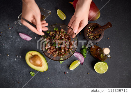 Woman mixing chopped tuna, cilantro and onion in a glass bowl cooking traditional tuna tartare 113839712