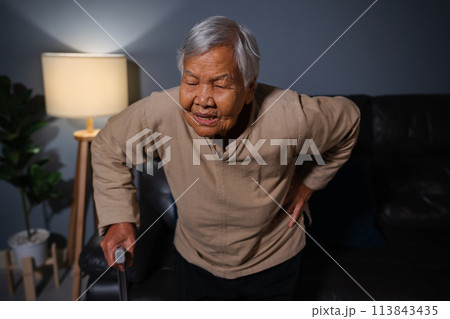 senior woman suffering from lower back pain in living room at night 113843435