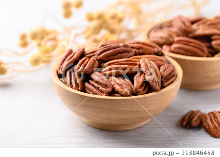 Raw peeled pecan nuts in wooden bowl on white table, Food ingredient 113846458