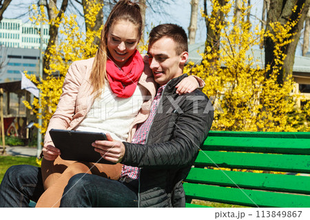 couple with tablet sitting on bench outdoor 113849867