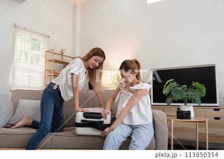 Young Asian woman packing clothes to the suitcase. Preparation for the summertime vacation. Two women are planning a trip and helping to prepare luggage to travel 113850354