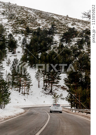 A vehicle navigates the snowy mountain road with caution 113850822