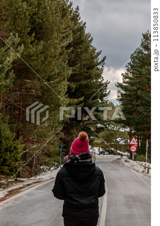 A person in a pink hat strolls on a snowy thoroughfare A person in a pink hat strolls on a snowy thoroughfare 113850833