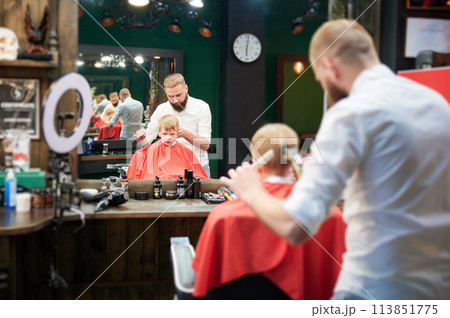 Barber using comb and shaver to cut hair. Professional hairdresser shaving little kid's nape. Barber using comb and shaver to cut hair. Professional hairdresser shaving little kid's nape. 113851775