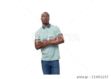 a young slender American man dressed in a T-shirt and jeans stands thoughtfully on a white 113852237