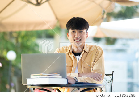 Pensive Student with Laptop Outdoors on University Grounds 113853289