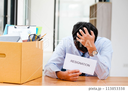 Man at desk with resignation letter, pondering his decision beside a packed box. 113853338