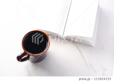 テーブルの上の開いた本とコーヒーカップで、コーヒーを飲みながら読書を楽しむイメージ 113854155